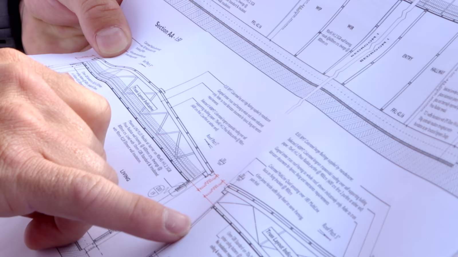 A hand pointing to a cross-section and floor plan on a printed New Zealand residential building plan